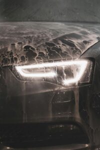 Detail shot of a car headlight covered in foam during a wash, showcasing cleanliness and care.